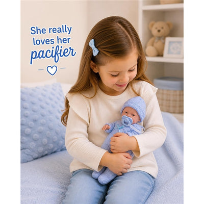 Young girl smiling while holding a JC Toys Mini La Newborn 9.5 all-vinyl baby doll dressed in a blue knit onesie and pacifier.