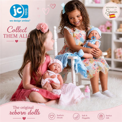 Two girls play with JC Toys La Newborn Real Girl Baby Dolls, one in a pink knit outfit, surrounded by accessories.