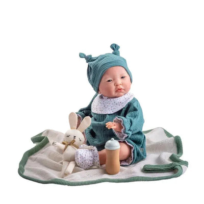 All-vinyl boy doll dressed in blue with a hat, holding a bunny and a bottle, placed on a patterned blanket.