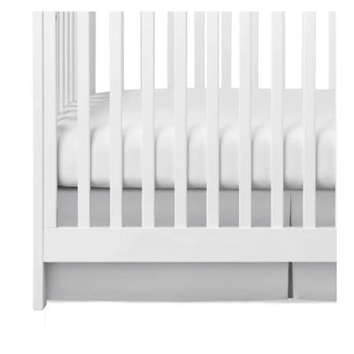 Gray pleated crib skirt styled under a white crib, complementing a white fitted mattress.