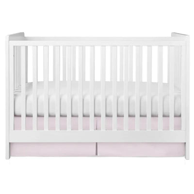 Pleated pink crib skirt draping beneath a white crib with a cushioned white mattress.