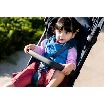 Young child sitting in a stroller with a Joolz Aer² foldable bumper bar, wearing a blue vest and pink sleeves.