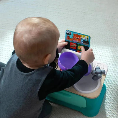 Child engaging with the Kids II - Be + Hape Magic Touch Kitchen, exploring interactive cooking features and a purple bowl.