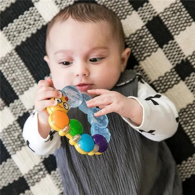 Infant playing with a colorful Teether-Pillar rattle, featuring multiple beads and a playful design, on a checkered blanket.