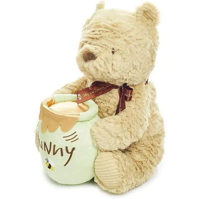 Plush Disney Classic Pooh bear holding a soft honey pot, featuring a ribbon and musical mechanism.
