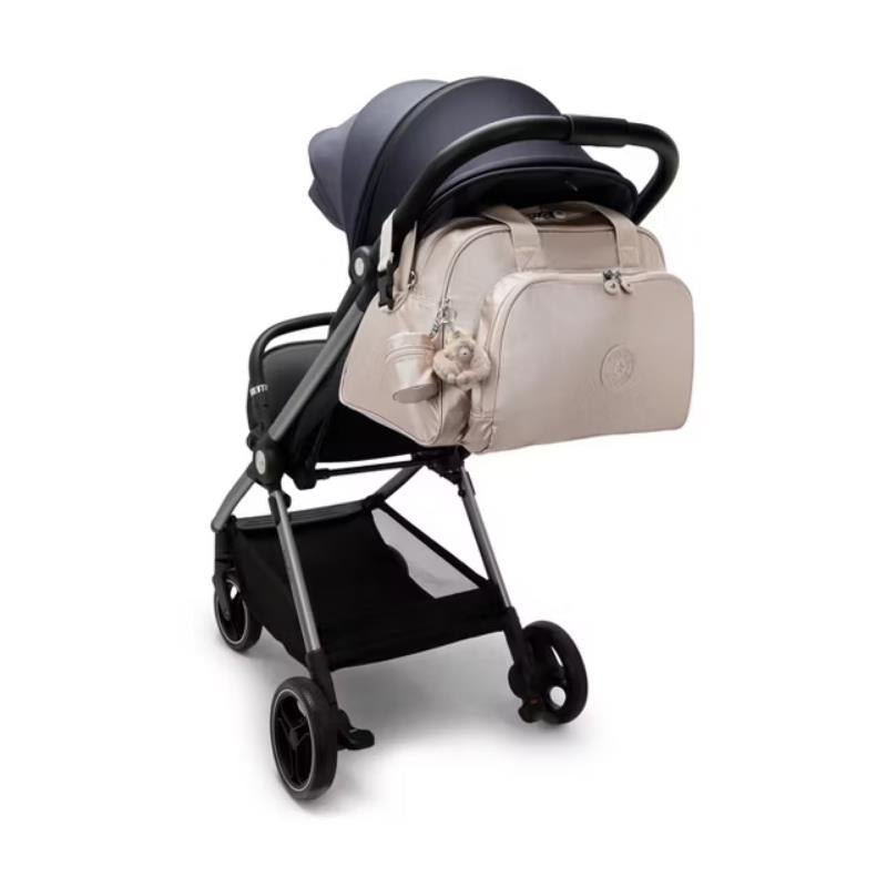 Kipling Camama Diaper Bag in Tiny Metallic Glow attached to a stroller, featuring a soft, neutral color and a charm.