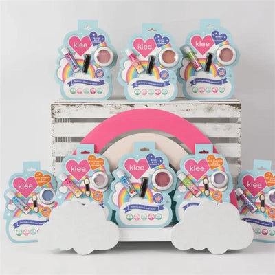 Klee Naturals Cotton Candy Whisper Blush and Lip Shimmer Set displayed on a rustic wooden crate with colorful packaging and decorative clouds.