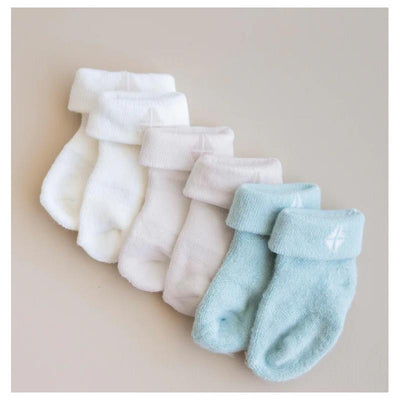 Three pairs of Kyte Baby socks in neutral colors: white, light gray, and sage green, each with a cuffed design.
