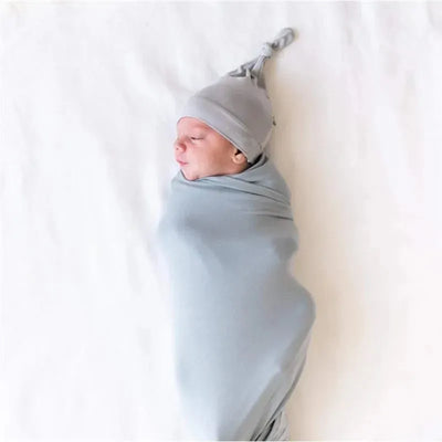 Bamboo baby knotted cap in Storm color worn by a swaddled newborn, resting on a soft white surface.