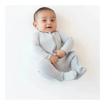 Neutral zippered footie in storm grey on a smiling baby seated against a white background.