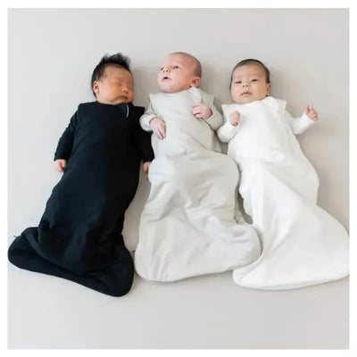 Three babies resting in bamboo sleep bags: one black, one grey, and one white, on a light background.