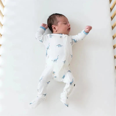 Zippered footie for babies featuring blue dinosaur prints, worn by an infant lying on a white crib mattress.