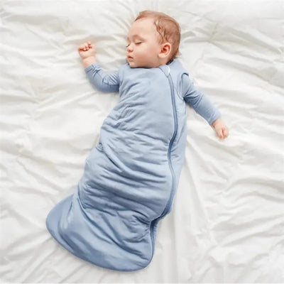 Baby peacefully sleeping in a slate-colored Kyte Baby Bamboo Sleep Bag 1.0 Tog, lying on a white blanket.