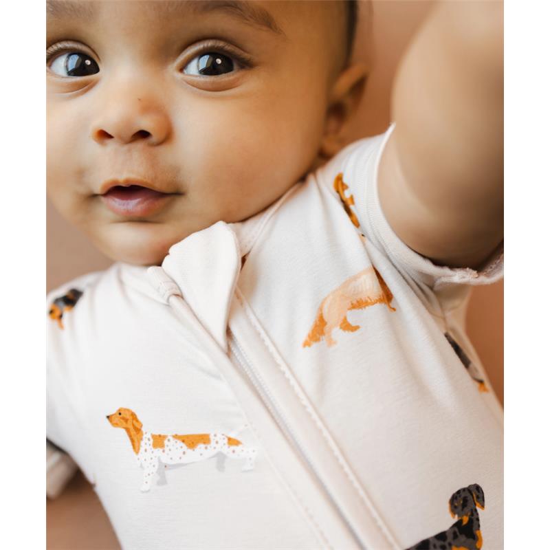 Infant wearing Kyte Baby Zipper Shortall Romper featuring colorful dachshund prints, with a cheerful expression.
