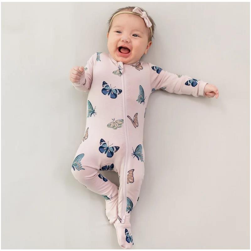 Smiling baby in a blush pink zippered footie covered in butterfly prints, lying on a light background.