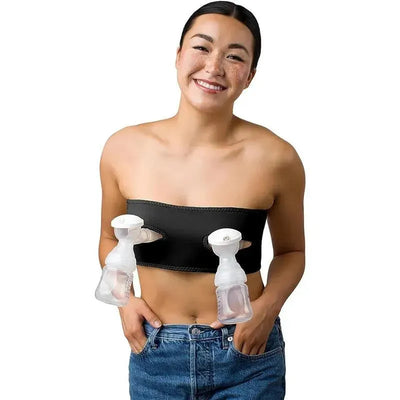 Black hands-free pumping and nursing bra worn by a smiling woman, with breast pumps attached on each side.