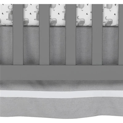 Gray linen crib skirt with white trim, designed for a crib, complementing a whimsical elephant-themed bedding.