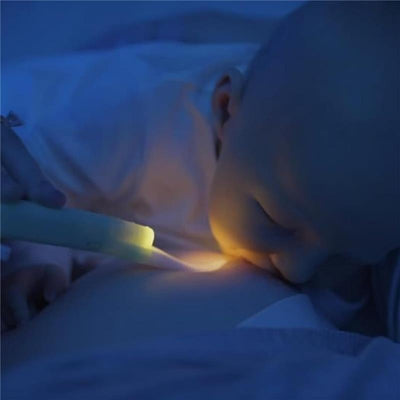A baby breastfeeding in a dimly lit room, illuminated by a Latchlight wearable baby night light held by an adult.