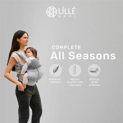 Mother wearing a Líllé Baby Complete All Seasons Carrier in Pebble Grey, holding a baby with text highlighting comfort and adjustability.