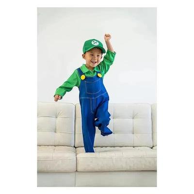 Child in a green and blue handyman costume with a hat, joyfully posing on a white sofa.