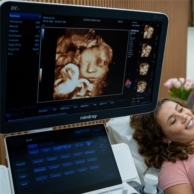 4D ultrasound screen displaying a 8K image of a fetus, with a smiling expectant mother nearby in a clinical setting.