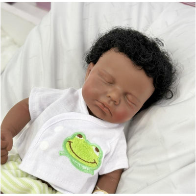 Full silicone African American baby doll with rooted hair, wearing a white outfit with a smiling frog design.