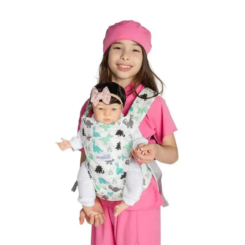 A girl in pink clothing holds a cuddly baby doll in a dinosaur-themed maternity carrier.