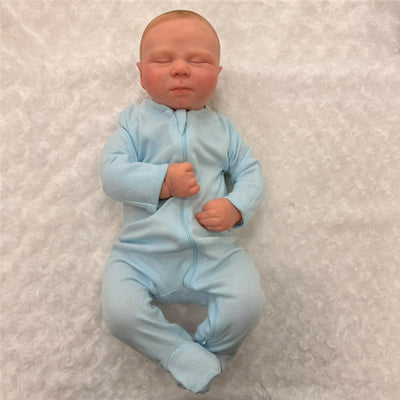 Macrobaby Reborn Doll named Charlie, featuring a realistic white vinyl face, closed eyes, and blue onesie, resting on soft fabric.