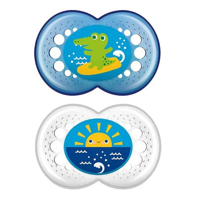 Two pacifiers featuring colorful designs: one with a green alligator on a surfboard and another with a smiling sun over waves.