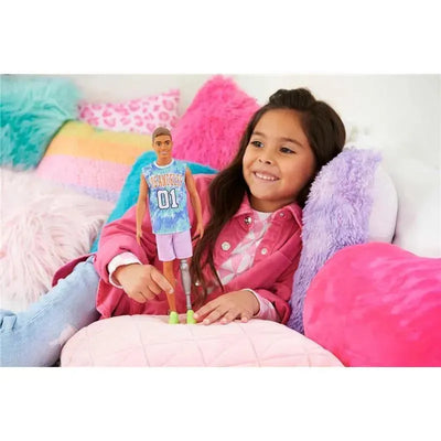 Barbie Ken Fashionista doll in a Los Angeles jersey, seated with a girl on colorful pillows, smiling.