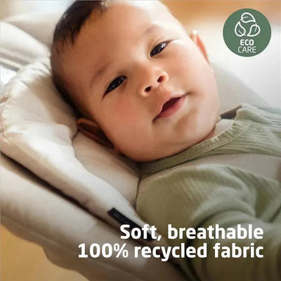 Baby in a high chair wearing a light green outfit, with a cushion that highlights soft, breathable, 100% recycled fabric.