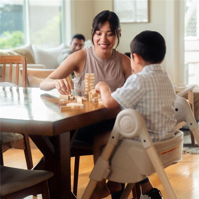 Mother and child playing a game with wooden blocks at a dining table, child seated in a Maxi-Cosi Minla high chair.