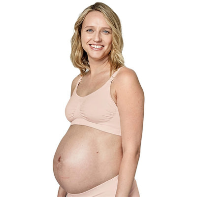 Pregnant woman smiling while wearing a peach-colored Medela seamless comfort bra.