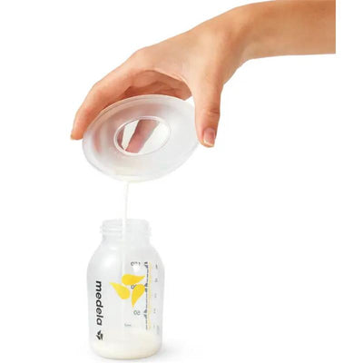 Medela milk collection shells pouring breast milk into a clear measuring bottle, showcasing the product in use.