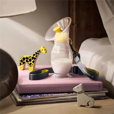 Medela Silicone Breast Milk Collector displayed on a pink surface, with milk inside, alongside toy giraffe and dog figures.
