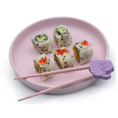 Chopsticks with a cat design resting on a pink plate containing five pieces of sushi rolls.