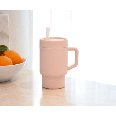 Melii Silicone Tumbler in light pink, 9 oz, with a removable lid and straw, beside a bowl of oranges.
