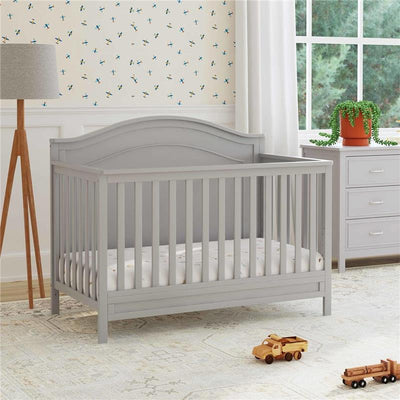 Gray Million Dollar Baby Charlie 4-In-1 Convertible Crib with slatted sides and a soft mattress, set in a bright nursery.