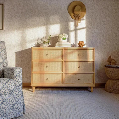 Honey-colored six-drawer dresser with cane accents, styled with books and decorative items, in a cozy room setting.