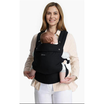 Momcozy black baby carrier worn by a smiling woman holding an infant, designed for newborns to toddlers.