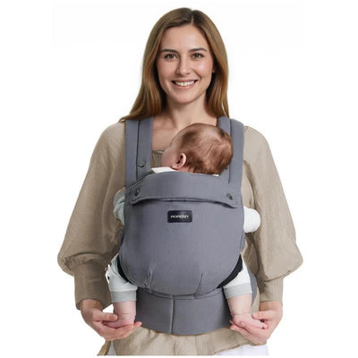 A woman smiles while wearing a grey Momcozy baby carrier that holds an infant securely against her chest.
