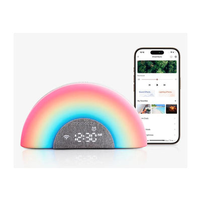 Dreamsync Smart Baby Sound Machine by Momcozy with rainbow light, clock display, and app interface on smartphone.