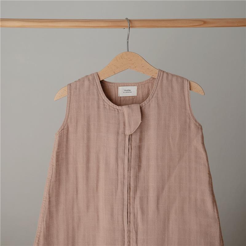100% organic cotton muslin baby wearable blanket in a natural, soft beige color displayed on a wooden hanger.