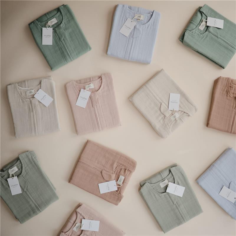 Mushie 100% organic cotton muslin baby wearable blankets in various pastel colors, neatly folded with tags.