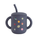 Mushie silicone training cup with a dark blue body, featuring colorful planet designs and a matching straw.