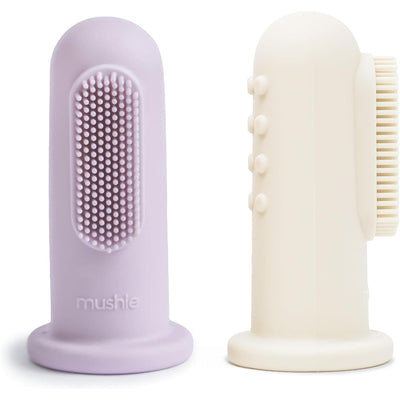 Soft lilac and ivory Mushie finger toothbrushes are shown, designed for gentle cleaning of teeth and gums.