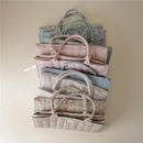 A stack of Mushie baby diaper caddies in various colors and floral patterns, designed for organizing newborn essentials.