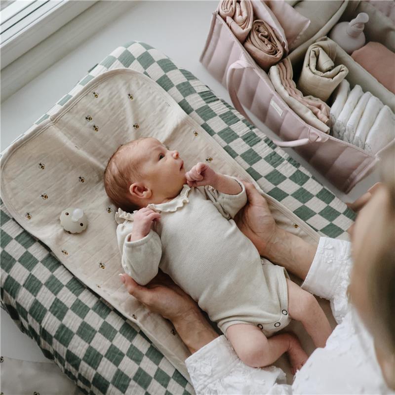 Newborn baby lying on a checkered changing mat with a diaper caddy in the background, filled with organized baby essentials.