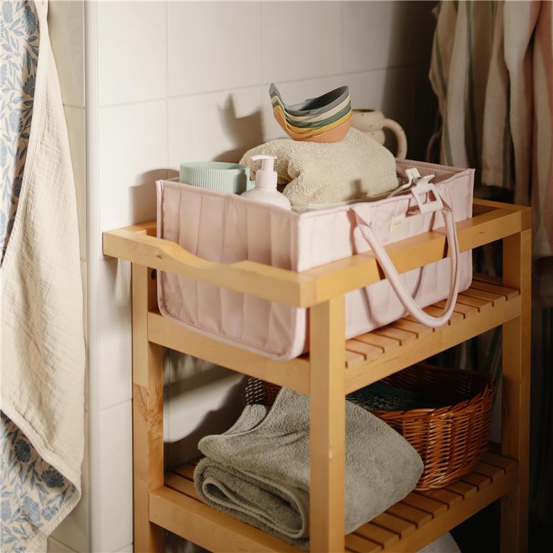 Pastel blooms Mushie Baby Diaper Caddy placed on a wooden shelf, filled with baby essentials like towels and a lotion bottle.