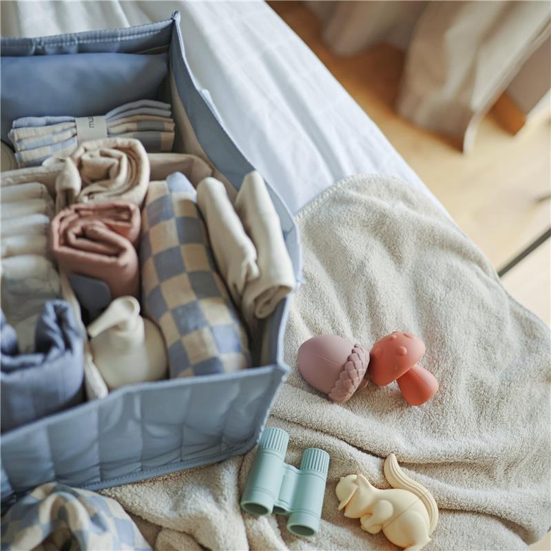Mushie Baby Diaper Caddy in Tradewinds color, filled with neatly rolled clothing, alongside colorful toys on a soft blanket.